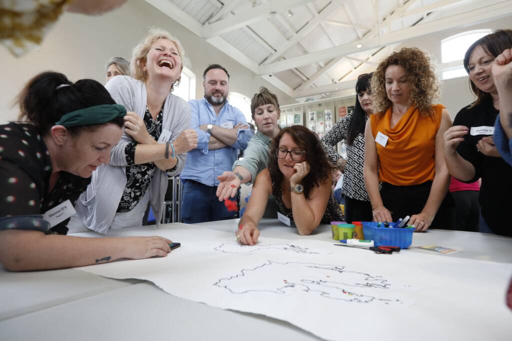 A group of adults lean over a table with black map outlines drawn on a white page.